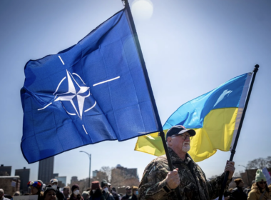 A man at the Hands Off protest against Trump in Minnesota is holding flags of Ukraine and NATO.